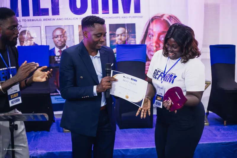 A Best Staff certificate being presented on stage as a colleague applauds